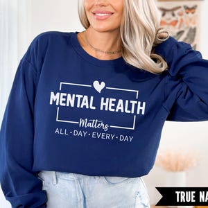 Peut inclure: Un sweat-shirt bleu marine avec le texte "MENTAL HEALTH Matters ALL DAY EVERY DAY" en blanc. Un c&oelig;ur blanc est au-dessus du mot "Matters". Les mots "TRUE NAVY" sont dans une banni&egrave;re noire en bas.