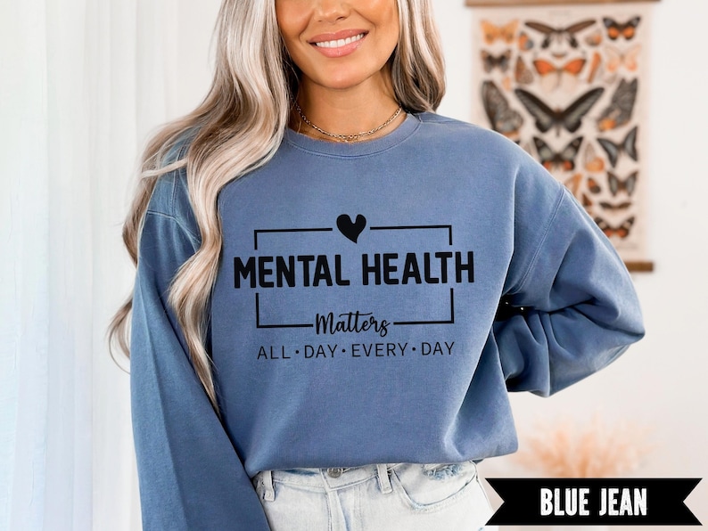 Peut inclure: Sweat-shirt bleu jean avec l'inscription noire "MENTAL HEALTH Matters ALL DAY EVERY DAY". Le motif comprend un symbole de c&oelig;ur au-dessus du mot "HEALTH".