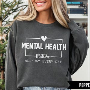 Peut inclure: Sweat-shirt gris fonc&eacute; avec l'inscription blanche "MENTAL HEALTH Matters ALL DAY EVERY DAY". Un c&oelig;ur blanc est au-dessus du mot "HEALTH". Le sweat-shirt est de style col rond.