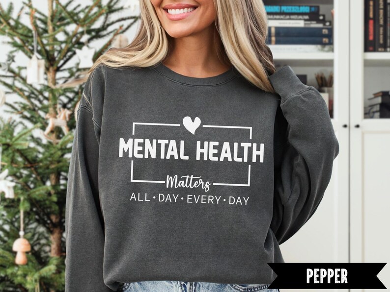 Peut inclure: Sweat-shirt gris fonc&eacute; avec l'inscription blanche "MENTAL HEALTH Matters ALL DAY EVERY DAY". Un c&oelig;ur blanc est au-dessus du mot "HEALTH". Le sweat-shirt est de style col rond.