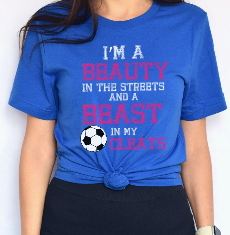 May include: A royal blue t-shirt with the text "I'm a beauty in the streets and a beast in my cleats" in white and pink lettering. A white soccer ball is centered below the text.
