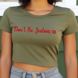 Puede incluir: Una camiseta verde recortada con el texto "Don't Be Jealous" en letras rojas y una impresi&oacute;n de labios rojos.