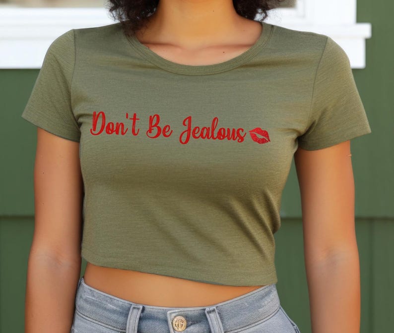 Puede incluir: Una camiseta verde recortada con el texto "Don't Be Jealous" en letras rojas y una impresi&oacute;n de labios rojos.