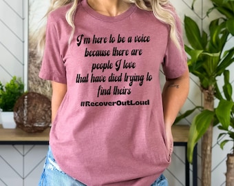 May include: Mauve t-shirt with black text: "I'm here to be a voice because there are people I love that have died trying to find theirs #RecoverOutLoud". The shirt is a crew neck and has short sleeves.