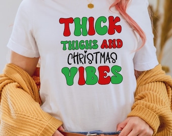 Puede incluir: Camiseta blanca con el texto "THICK THIGHS AND CHRISTMAS VIBES" en letras rojas y verdes.
