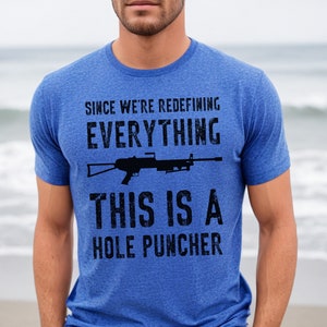May include: A blue t-shirt with a distressed graphic of a rifle and the text "Since we're redefining everything, this is a hole puncher."
