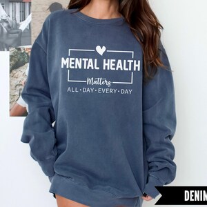 Peut inclure: Sweat-shirt bleu denim avec l'inscription blanche "MENTAL HEALTH Matters ALL DAY EVERY DAY" et un symbole de c&oelig;ur. Le sweat-shirt est de coupe d&eacute;contract&eacute;e.