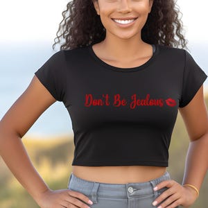 Puede incluir: Un top corto negro con mangas cortas y el texto "Don't Be Jealous" en rojo con una impresi&oacute;n de l&aacute;piz labial rojo.