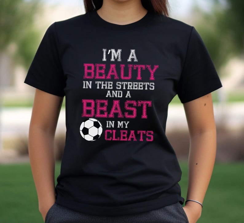 May include: Black t-shirt with pink text that reads "I'm a Beauty in the Streets and a Beast in my Cleats". A white soccer ball is next to the text.