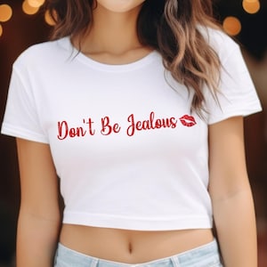 Puede incluir: Top corto blanco con el texto "Don't Be Jealous" en letras rojas y una impresi&oacute;n de labios rojos con purpurina.