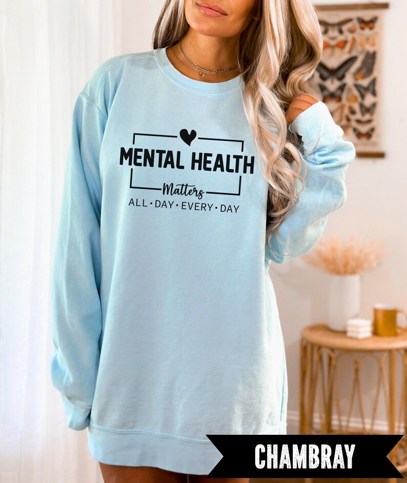 Peut inclure: Un sweat-shirt bleu clair avec le texte "MENTAL HEALTH Matters ALL DAY EVERY DAY" en noir. Un c&oelig;ur noir est au-dessus du mot "Matters". Le mot "CHAMBRAY" est dans une banni&egrave;re noire en bas.