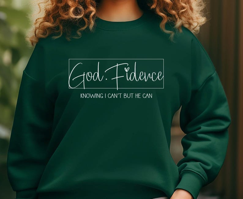 以下が含まれることがあります： 白い書体で「God. Fidence」と書かれた濃い緑色のスウェットシャツ。テキストは白い長方形で囲まれています。長方形の下には「Knowing I can't but He can.」というテキストがあります。