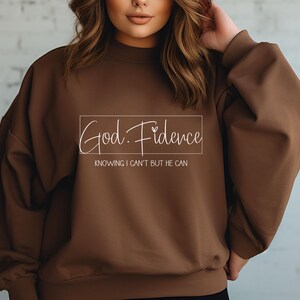 以下が含まれることがあります： 「God. Fidence」と「Knowing I can't but He can」という文字が書かれた茶色のスウェットシャツです。