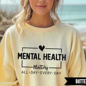 Peut inclure: Un sweat-shirt jaune clair avec l'inscription noire "MENTAL HEALTH Matters ALL DAY EVERY DAY". Un c&oelig;ur noir est au-dessus du mot "HEALTH". Le mot "BUTTER" est dans une banni&egrave;re noire en bas.
