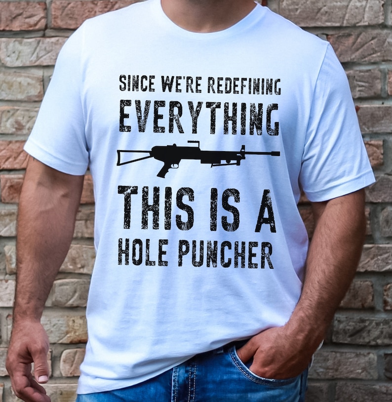 May include: White t-shirt with a black graphic of a machine gun and the text "Since we're redefining everything, this is a hole puncher."