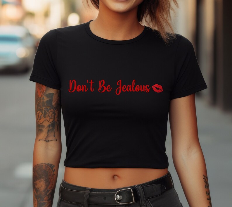 Puede incluir: Camiseta negra recortada con texto rojo que dice "Don't Be Jealous" y una impresi&oacute;n de labios rojos.