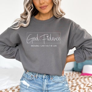 以下が含まれることがあります： グレーのトレーナーに「God. Fidence」という文字と「Knowing I can't but He can」というフレーズが白文字で書かれています。