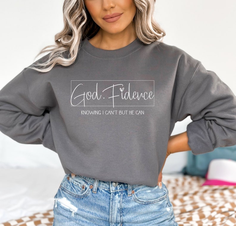 以下が含まれることがあります： グレーのトレーナーに「God. Fidence」という文字と「Knowing I can't but He can」というフレーズが白文字で書かれています。