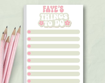 Puede incluir: Un bloc de notas con el texto "Faye's Things To Do" en rosa y blanco. El bloc de notas tiene un fondo verde claro con líneas horizontales y círculos rosas. Varios lápices rosas están en el lado izquierdo del bloc de notas.