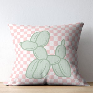 May include: Square throw pillow featuring a light green balloon dog design on a pink and white checkered background. The pillow is a decorative item, suitable for a living room or bedroom.