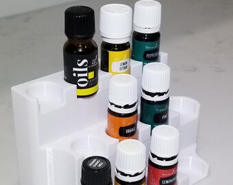 Puede incluir: Organizador de plástico blanco con ocho ranuras para botellas de aceites esenciales. El organizador está lleno de varias botellas de aceites esenciales, incluyendo limón, naranja, pino y limoncillo.