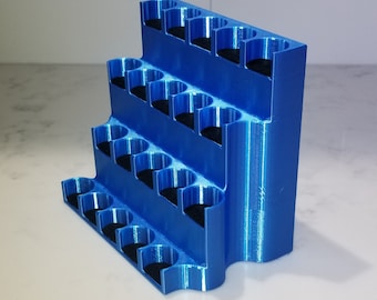 Puede incluir: Un organizador de plástico azul con varios niveles y ranuras para guardar objetos pequeños. El organizador está hecho de plástico impreso en 3D y tiene un acabado liso y brillante.