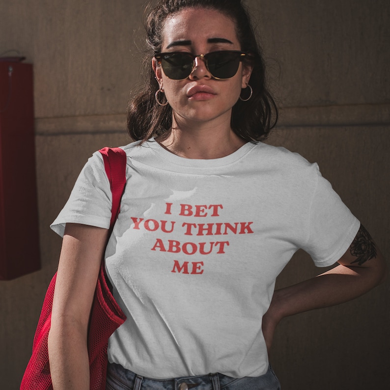Op de afbeelding: Wit T-shirt met rode tekst die "I bet you think about me" zegt.
