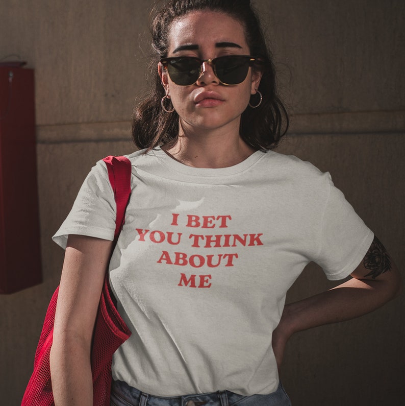 Op de afbeelding: Wit T-shirt met rode tekst die "I bet you think about me" zegt.