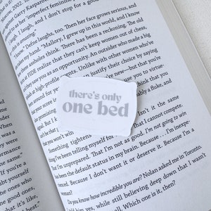 Op de afbeelding: Een close-up van een boekpagina met de tekst "there's only one bed" gedrukt op een witte sticker. De tekst is in een vet, sans-serif lettertype. De sticker is geplaatst over een paragraaf tekst over de ervaring van een vrouw in de schaakwereld.
