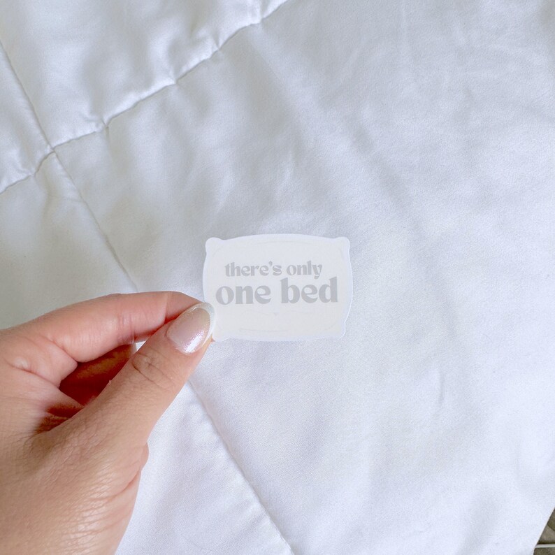 Op de afbeelding: Witte sticker in de vorm van een kussen met de tekst "there's only one bed" in wit.