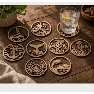 May include: A collection of laser-cut wooden coasters with various ocean-themed designs, including a lighthouse, waves, an anchor, a whale tail, a turtle, a seahorse, a seashell, and dolphins. A glass of water with a lemon slice sits on one coaster.