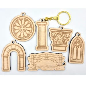 Peut inclure: Ensemble de porte-clés en bois avec des motifs architecturaux. Les porte-clés représentent une fenêtre ronde, une colonne, un chapiteau, une arche, un pont et une fenêtre gothique. Ils sont reliés par un porte-clés doré.