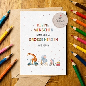 K&ouml;nnte beinhalten: Eine Gru&szlig;karte mit dem Text "KLEINE MENSCHEN BRAUCHEN SO GROSSE HERZEN WIE DEINS!" und Illustrationen einer Giraffe auf einem Roller, eines Elefanten auf einem Fahrrad und eines Igels in einem Wagen. Buntstifte umgeben die Karte.