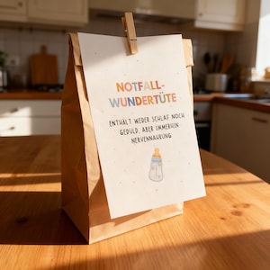 May include: A brown paper bag with a white card clipped to it. The card has text in multiple colors and a baby bottle illustration. The text reads "NOTFALL-WUNDER-T&Uuml;TE" and other German text. The bag is on a wooden surface.