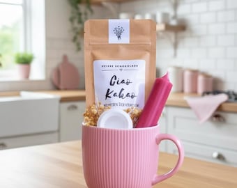 May include: A pink ribbed mug filled with a brown paper packet, a pink candle, and dried flowers. The packet has text that reads "HEISSE SCHOKOLADE" and "Ciao Kakao". A white lid is also inside the mug.