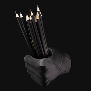 Peut inclure: Un porte-crayons en forme de main noire avec un tas de crayons noirs qui dépassent du haut.
