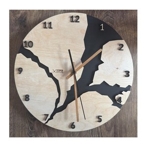 Può includere: Un orologio rotondo in legno con accenti dipinti di nero. Il quadrante dell'orologio è diviso in due sezioni, una in legno chiaro e l'altra nera. I numeri da 1 a 12 sono visualizzati attorno al quadrante dell'orologio. Le lancette dell'orologio sono nere e marroni.