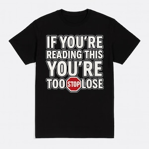 May include: Black t-shirt with white text that reads "IF YOU'RE READING THIS YOU'RE TOO STOP LOSE". The word "STOP" is inside a red stop sign graphic. The shirt is a classic crew neck style.