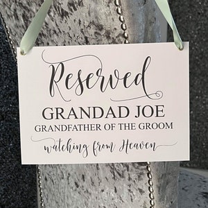 Może przedstawiać: Biały znak z czarnym tekstem, na którym napisano "Zarezerwowane Grandad Joe Dziadek Pana Młodego obserwujący z nieba". Znak jest zawieszony na szarym aksamitnym krześle z jasnozieloną wstążką.