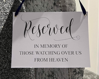 Könnte beinhalten: Ein weißes Schild mit schwarzem Text, der in Kursivschrift "Reserviert" lautet. Unter dem Wort "Reserviert" steht der Text "In Gedenken an diejenigen, die von oben über uns wachen".
