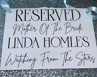 Könnte beinhalten: Ein weißes Schild mit schwarzem Text, der "RESERVED Mother Of The Bride LINDA HOMLES Watching From The Stars" lautet. Das Schild ist mit einem hellblauen Band verziert.