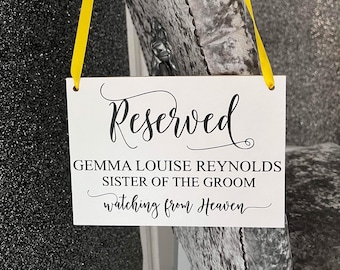 Könnte beinhalten: Ein weißes Schild mit schwarzem Text, auf dem steht "Reserviert Gemma Louise Reynolds Schwester des Bräutigams schaut vom Himmel". Das Schild ist mit einem gelben Band an einem grauen Stuhl befestigt.