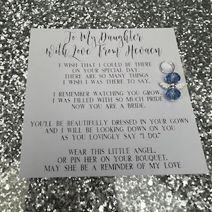 May include: A white card with a message to a daughter from her mother in heaven. The card says "To My Daughter With Love From Heaven" and includes a message about the daughter's wedding day. The card also includes a small blue angel charm with silver wings.