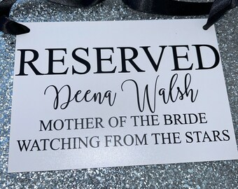Könnte beinhalten: Ein weißes Schild mit schwarzem Text, auf dem steht "RESERVED Deena Walsh MOTHER OF THE BRIDE WATCHING FROM THE STARS". Das Schild ist mit einem schwarzen Band gebunden.