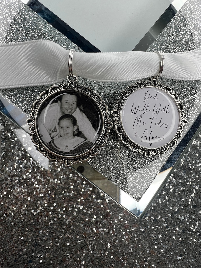 May include: Two silver charm pendants with a white ribbon. One pendant has a black and white photo of a father and daughter. The other pendant has the text "Dad Walk With Me Today & Always" in black script.
