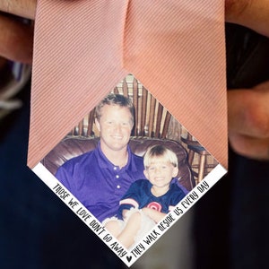 May include: A pink tie with a photograph of a father and son. The photo is in a white frame with the text "Those we love don't go away, they walk beside us every day".