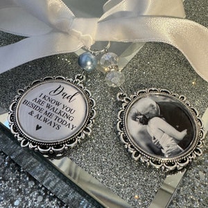 May include: A silver charm with a white ribbon and a photo of a couple in a silver frame. The charm also has a silver frame with the text "Dad I know you are walking beside me today & always" with a heart.