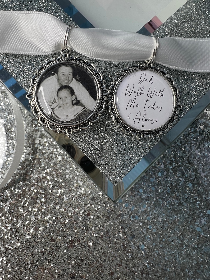 May include: Two silver charms with a white satin ribbon. One charm has a black and white photo of a father and daughter. The other charm has the text "Dad Walk With Me Today & Always".