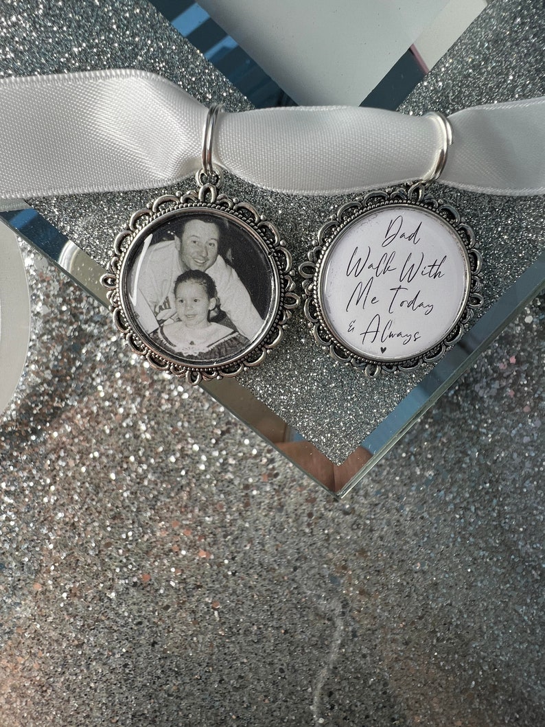 May include: Two silver charm pendants with a white satin ribbon. One pendant features a black and white photo of a father and daughter. The other pendant has the text "Dad Walk With Me Today & Always" in white script.