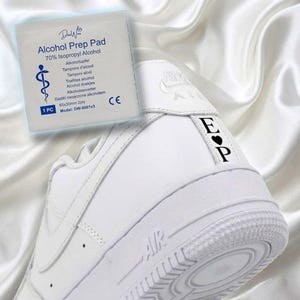 May include: White athletic shoe with the letters "EP" and a heart symbol on the heel. An alcohol prep pad is in the background. The prep pad has text that reads "Alcohol Prep Pad" and "70% Isopropyl Alcohol".